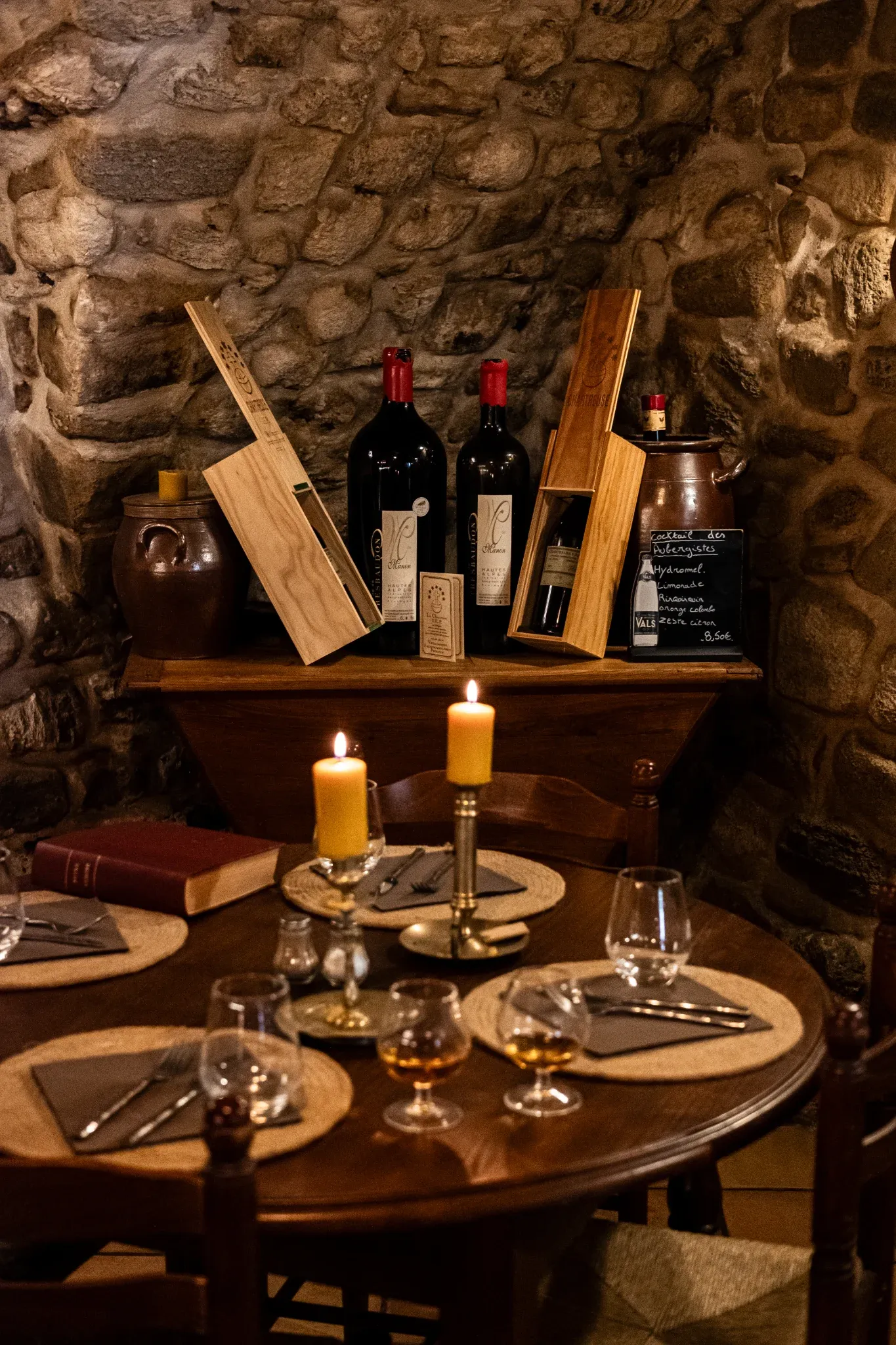 Une table avec deux verres de cognac. Au fond il y a un meuble avec plusieurs bouteille de vin.